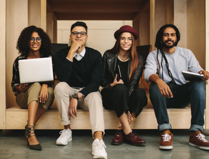 Four young adults sitting and smiling at the camera holding laptops