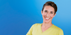 Women wearing a yellow t-shirt against a blue background smiles at the camera