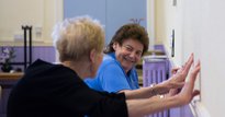 Two elderly women exercising against a wall