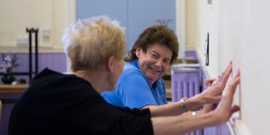 Two elderly women exercising against a wall