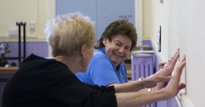 Two elderly women exercising against a wall