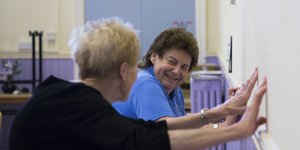 Two elderly women exercising against a wall