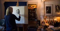 Woman with blonde hair drawing a young girl on an easel