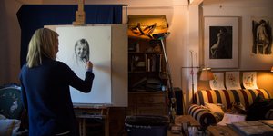 Woman with blonde hair drawing a young girl on an easel