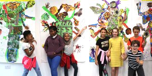 Group of young children smiling against a wall of colourful art
