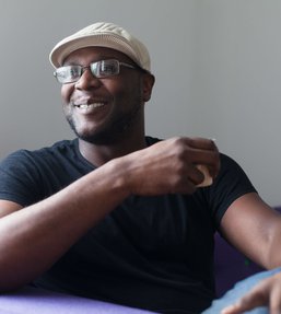 Man with glasses wearing a white cup and black t-shirt holding a mug and smiling