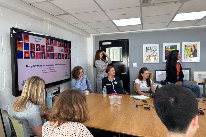 Group of people sat around a desk listening to a speaker out of shot
