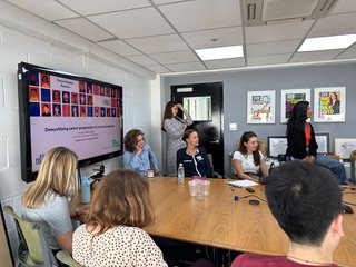 Group of people sat around a desk listening to a speaker out of shot
