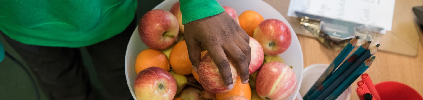 Child's hand reaching into a bowl of apples