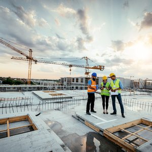 Construction workers reviewing plans at a large residential housing development site with cranes and new buildings under construction