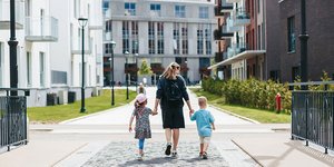 Parent walking with two children through a modern residential housing neighbourhood.