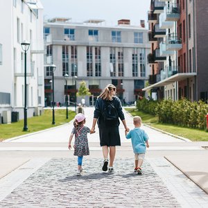 Parent walking with two children through a modern residential housing neighbourhood.