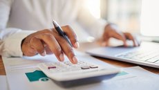 Stock image of someone in a shirt using a calculator and a laptop