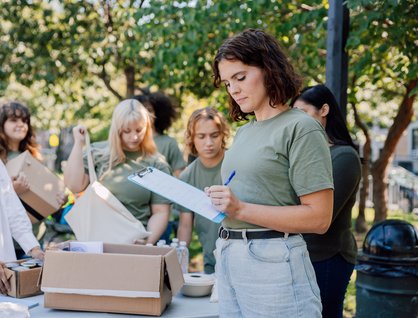 Woman writing on a clipboard with other women behind her preparing to distribute food and water