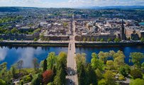 Birds eye view of a river, with lots of trees on one side and buildings on the other, with a road bridge going across