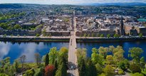 Birds eye view of a river, with lots of trees on one side and buildings on the other, with a road bridge going across